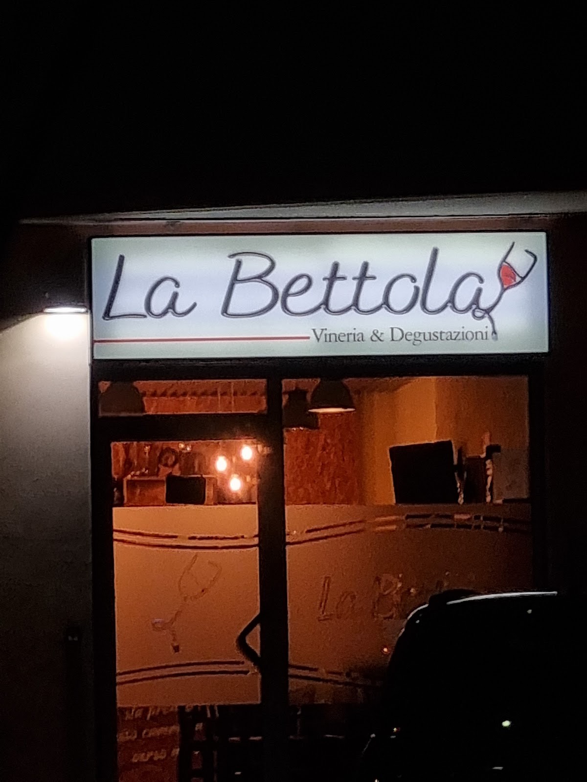 L'insegna illuminata di La Bettola, Vineria e Degustazioni, la sera